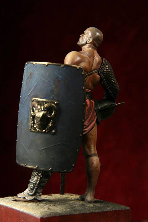 figura de un Gladiador en posici&oacute;n de descanso despu&eacute;s de haber ganado un combate, mirando hacia el  p&uacute;blico que llena el aforo en actitud desafiante.