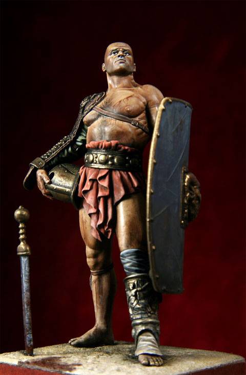 figura de un Gladiador en posici&oacute;n de descanso despu&eacute;s de haber ganado un combate, mirando hacia el  p&uacute;blico que llena el aforo en actitud desafiante.